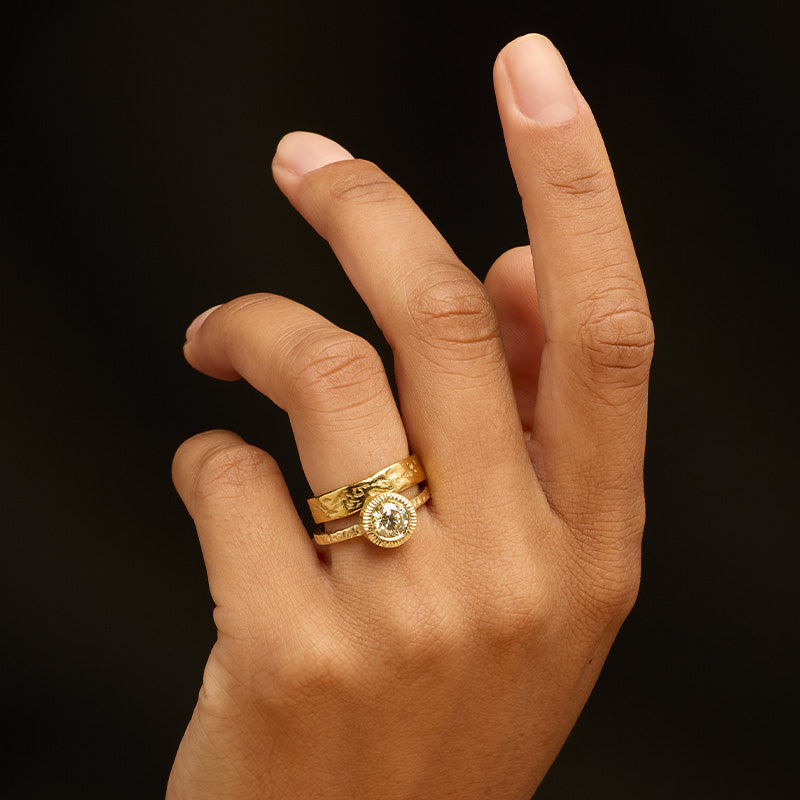 Magma Band paired with Aeon Diamond Ring - 9kt solid yellow gold 5mm band with a molten-like textured finish stacked with a 14kt solid yellow gold ring with a subtle textured finish, featuring a radiant 1ct round faceted light yellow diamond gemstone in a hand-etched bezel setting. Worn on the model's ring finger to suggest an alternative engagement or wedding ring stack.