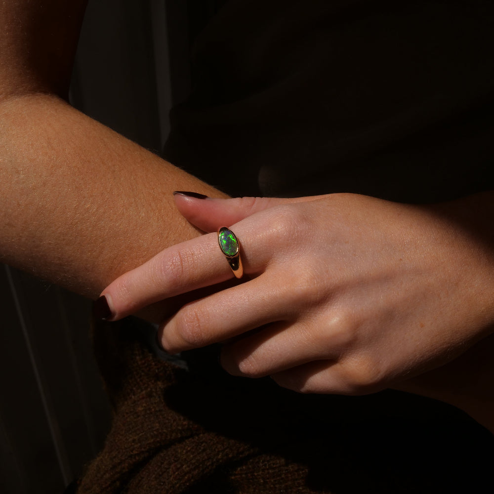 A close-up of hand wearing a gold signet opal ring