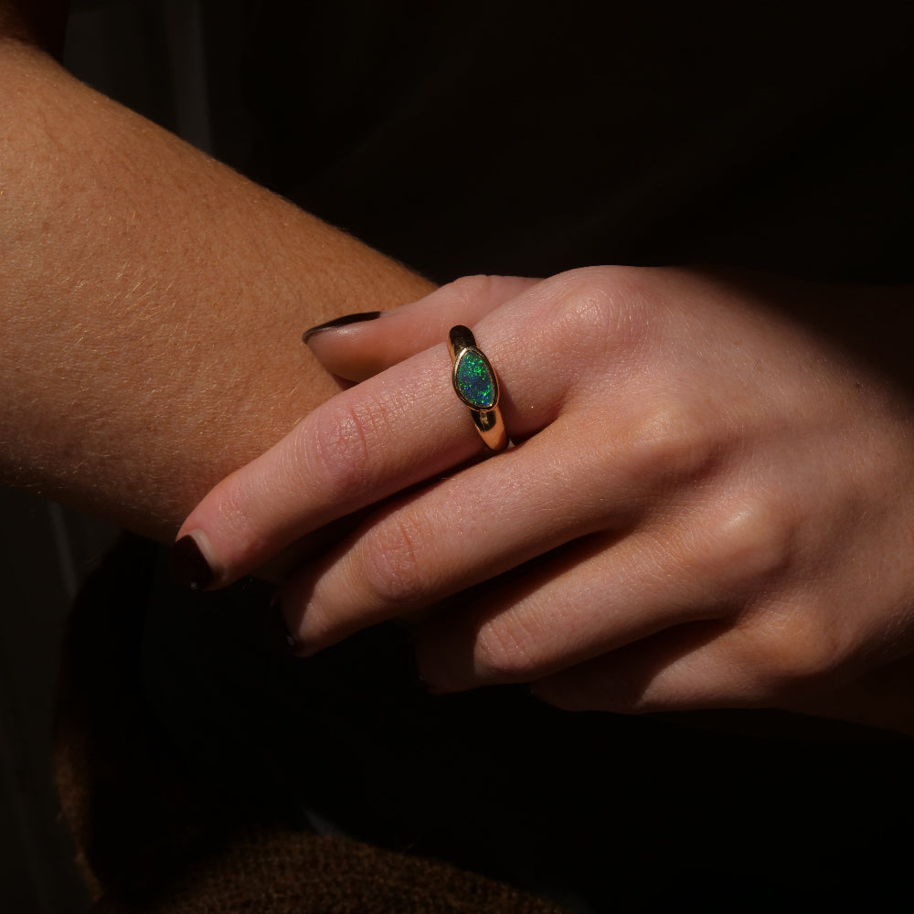 A close-up of a hand wearing a green blue opal ring