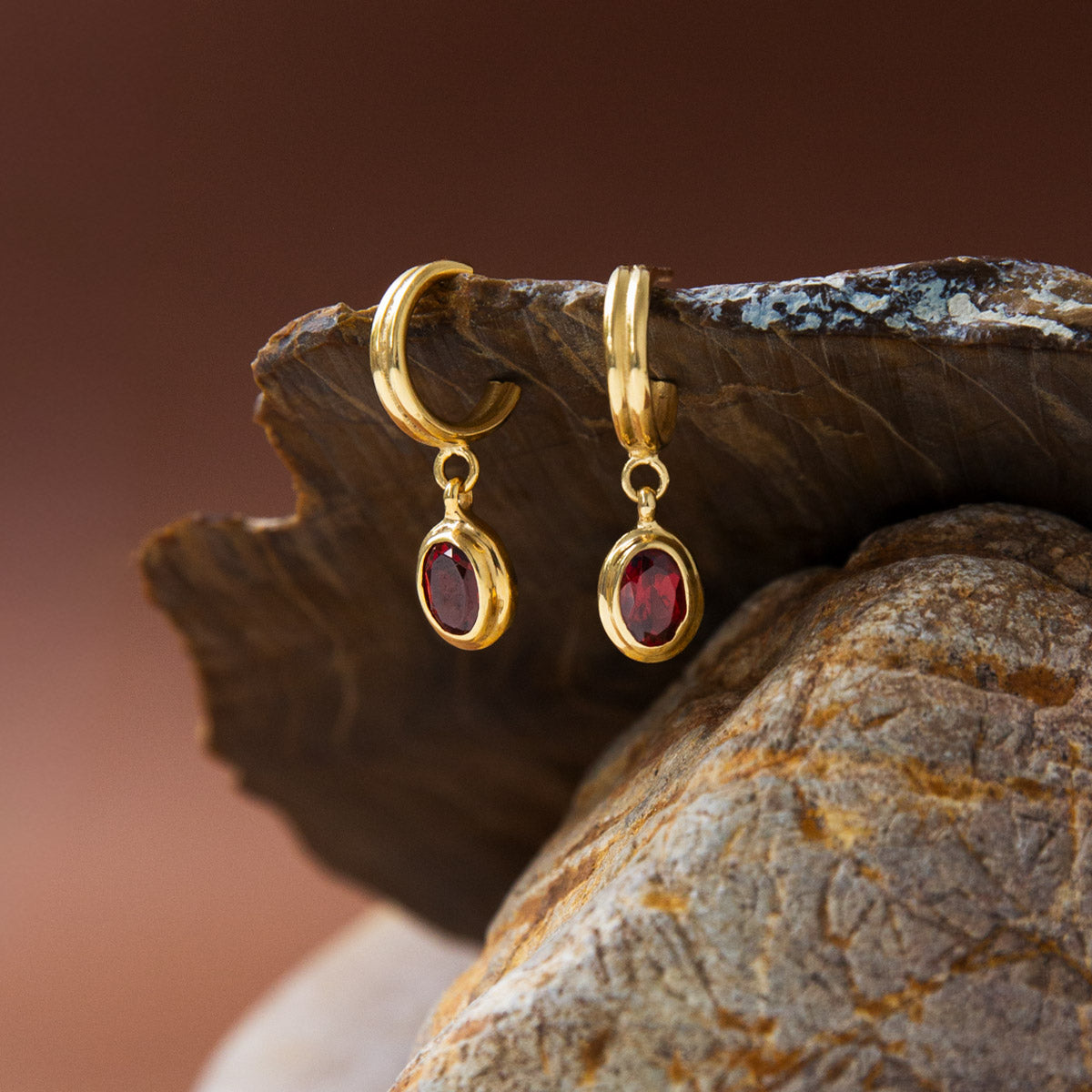 Gold earrings with red gemstones on a stone surface